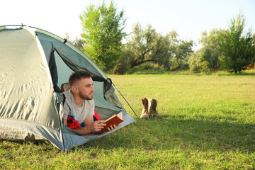 Sticker - Young man in sleeping bag with book lying inside camping tent