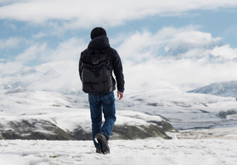 Wall Mural - a man with backpack walking on snow, trekking in winter