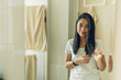 © Sevendeman - Happy Asian woman is combing her hair on the mirror of the bathroom.