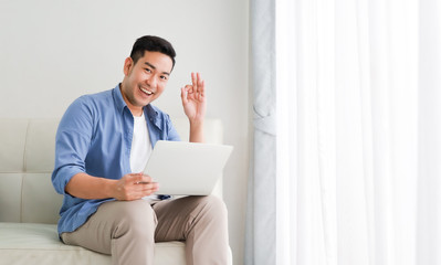 Asian handsome man working with laptop computer   in living room happy and smile face