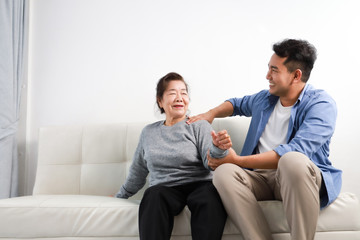 Wall Mural - Asian senior woman mother and young man son in blue shirt massage his mother in living room