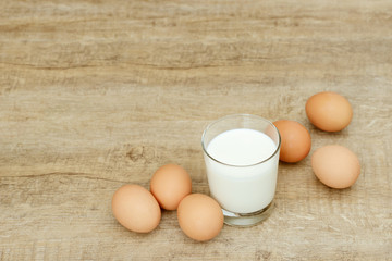 glass milk and brown eggs lying on wooden table