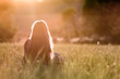 Back view of a woman with long hair sitting outdoors in sunlight enjoying nature.