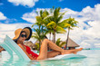 © Maridav - Luxury pool vacation woman sunbathing in lounging chair of high end hotel swimming pool holiday resort for summer getaway. Lady with sun hat and red swimsuit in water lounger.