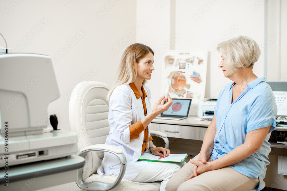 Senior woman patient talking with female ophthalmologist during a medical consultation at the ophthalmologic office. Doctor offering eye medcine for a patient - obrazy, fototapety, plakaty 