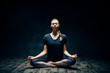 © GVS - Young attractive woman practicing yoga sitting in lotus pose and meditating in dark room