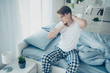 © deagreez - Portrait of upset sad man sit on bed wake up feel neck ache muscle tension have uncomfortable sleep wear checkered white plaid pajama in house indoors