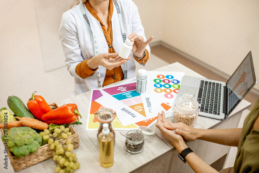 Nutritionist with young woman client talking about meal plan and healthy products during a medical consultation in the office - obrazy, fototapety, plakaty 