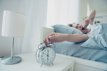 I need more sleep. Portrait of fatigued blonde haired man lying in bed yawning trying to awake have difficult day yesterday ignore ringing bell clock alarm in house indoors