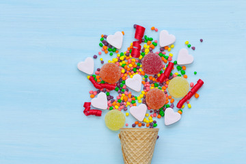 Wall Mural - Waffle cone with colorful candies on a blue background.