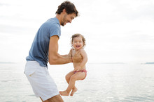 Father Holding Laughing Baby Girl At Beach