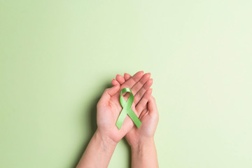 World mental health day concept. Green awareness ribbon in female hands on a green background.