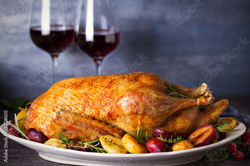 Baked duck with potatoes, plums, rosemary and thyme, close-up on plate, two glasses of red wine. Horizontal, room for text, copy space