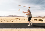 Fototapeta  - Funny overweight man chasing the hot dog on the stick through the empty road with copy space