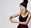 © Dmitry Lobanov - Portrait of stylish sporty blonde woman in sport vest and purple winter hat standing looking at her smart watches fitbit