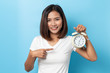 © suriya - Portrait of confused asian young girl holding alarm clock isolated on blue background