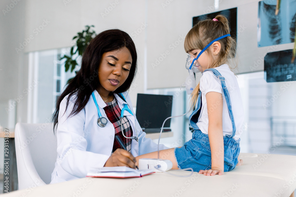 Young African female Doctor helping to little girl with nebulizer mask ...