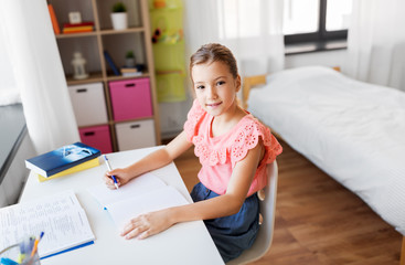 children, education and learning concept - student girl with book writing to notebook at home