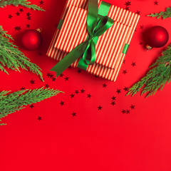 Wall Mural - Christmas background. Gift with green ribbon red balls christmas tree branches confetti stars on red background top view. New Year presents Festive decorations Flat lay Xmas holiday 2020 celebration