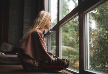 teenager girl with long blonde hair sits on a windowsill