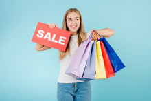 Smiling Happy Blonde Girl With Sale Sign And Colorful Shopping Bags Isolated Over Blue