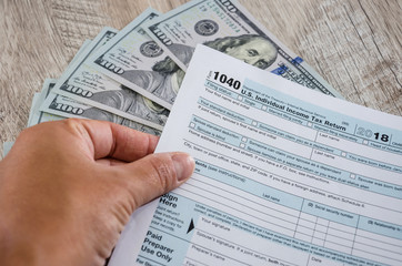 tax form 1040  in a hand on a background of dollars. Close-up.