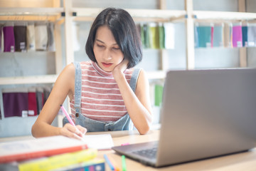 Young Asian woman using laptop computer and tablet PC to working in the modern co working space