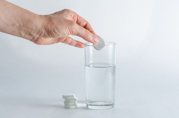 Wall Mural - A hand holding effervescent soluble calcium tablet or vitamin C is placed in a glass of water. Health.The concept of a healthy lifestyle, prevention of vitamin deficiency. Isolated on white background