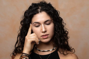 A stunning young brunette woman poses for a portrait, holding her finger against her head as she pauses for thoughts, lost in dreams contemplating life.