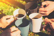 A group of young people holding mugs of coffee and clink them while in nature on a Sunny day