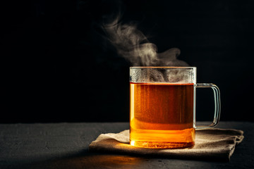 The process of brewing tea, pouring hot water from the kettle into the Cup, steam coming out of the mug, water droplets on the glass, black background