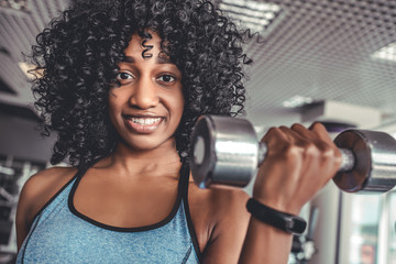 Wall Mural - Happy healthy young African American woman working out in a gym with a pair of dumbbells