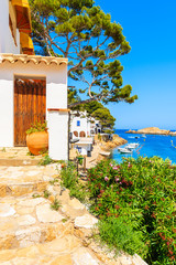 Wooden door of a white house decorated with flowers and view of beach in Sa Tuna fishing village, Costa Brava, Catalonia, Spain