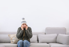 Young Man Wearing Warm Clothes Freezing On Sofa At Home. Air Conditioner Malfunction