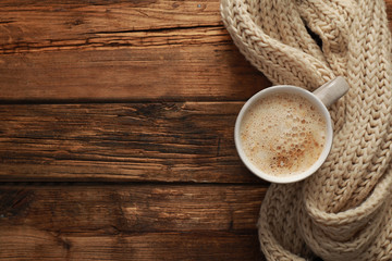 Top view of coffee and knitted scarf on wooden table, space for text. Cozy winter