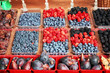 Fresh blueberries, raspberries, blackberries, figs and dry plums displayed in plastic containers on an outdoor market stall