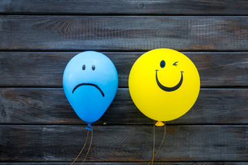 Wall Mural - Treat depression concept. Balloons with sad and smiling faces on dark wooden background top view