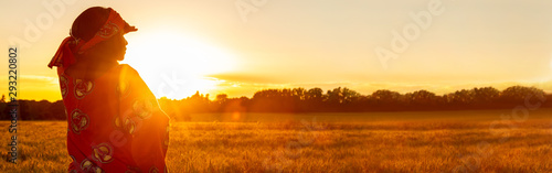 African woman in traditional clothes in field of crops at sunset or sunrise pano Tableau sur Toile