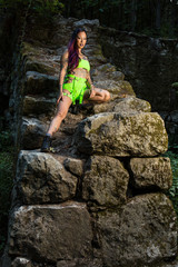 Wall Mural - Asian tattooed woman in neon rave clothing poses on an abandoned rock wall in the forest