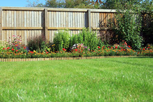 Shrubs And Flowers In A Border With A Grass Lawn Surrounded By A Wooden Fence.