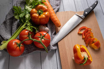 fresh vegetables on a light kitchen table. sliced paprika, orange carrot, two-tone paprika, red tomato and salad with knife on the kitchen table