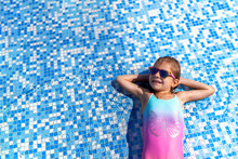 Little Girl In Sunglasses And Hat With Unicorn In Outdoor Swimming Pool Of Luxury Resort On Summer Vacation On Tropical Beach Island. Healthy Outdoor Sport Activity For Children. Kids Beach Fun