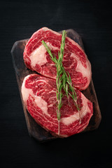 Wall Mural - Ideal raw rib eye beef steak with rosemary on black wooden background, top view and copy space