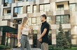 © bodnarphoto - Stylish young people guy and girl standing on the street against the backdrop of a modern building and talking, street portrait of beautiful young people talking outdoors.