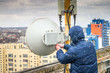 © Климов Максим - Man performs the maintenance of a radio-relay mobile base station in snowy weather. A technician repairs a wireless data transmitter in snowfall. Winter repair of telecommunications equipment.
