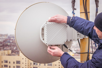 A man performs maintenance and repair of a powerful radio relay base station of mobile communication. A technician is repairing a wireless data transmitter on the roof of a city building. 