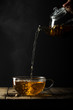 © The Picture Pantry - Hot tea being poured from a teapot in to a cup and saucer on a dark background