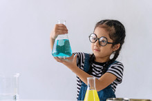 Little 6s Cute Girl With Microscope Holding Laboratory Bottle With Water Experiment Study Scientists At School. Education Science Concept.