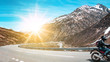 Motorrad fährt auf Passstraße in den Alpen - Panorama Berge mit Sonnenschein