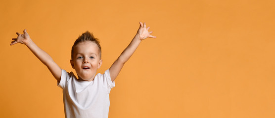 young boy kid in white t-shirt celebrating happy smiling laughing with hands spreading up on yellow